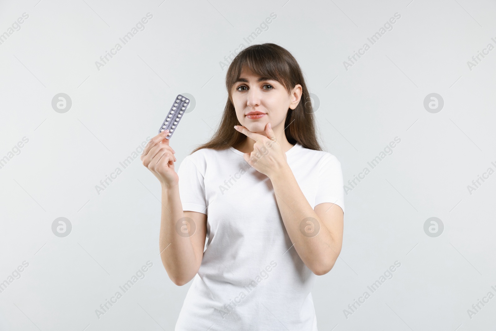 Photo of Young woman with blister of contraceptive pills on light background