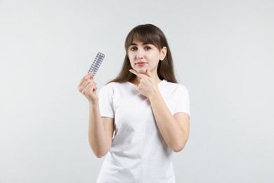 Photo of Young woman with blister of contraceptive pills on light background