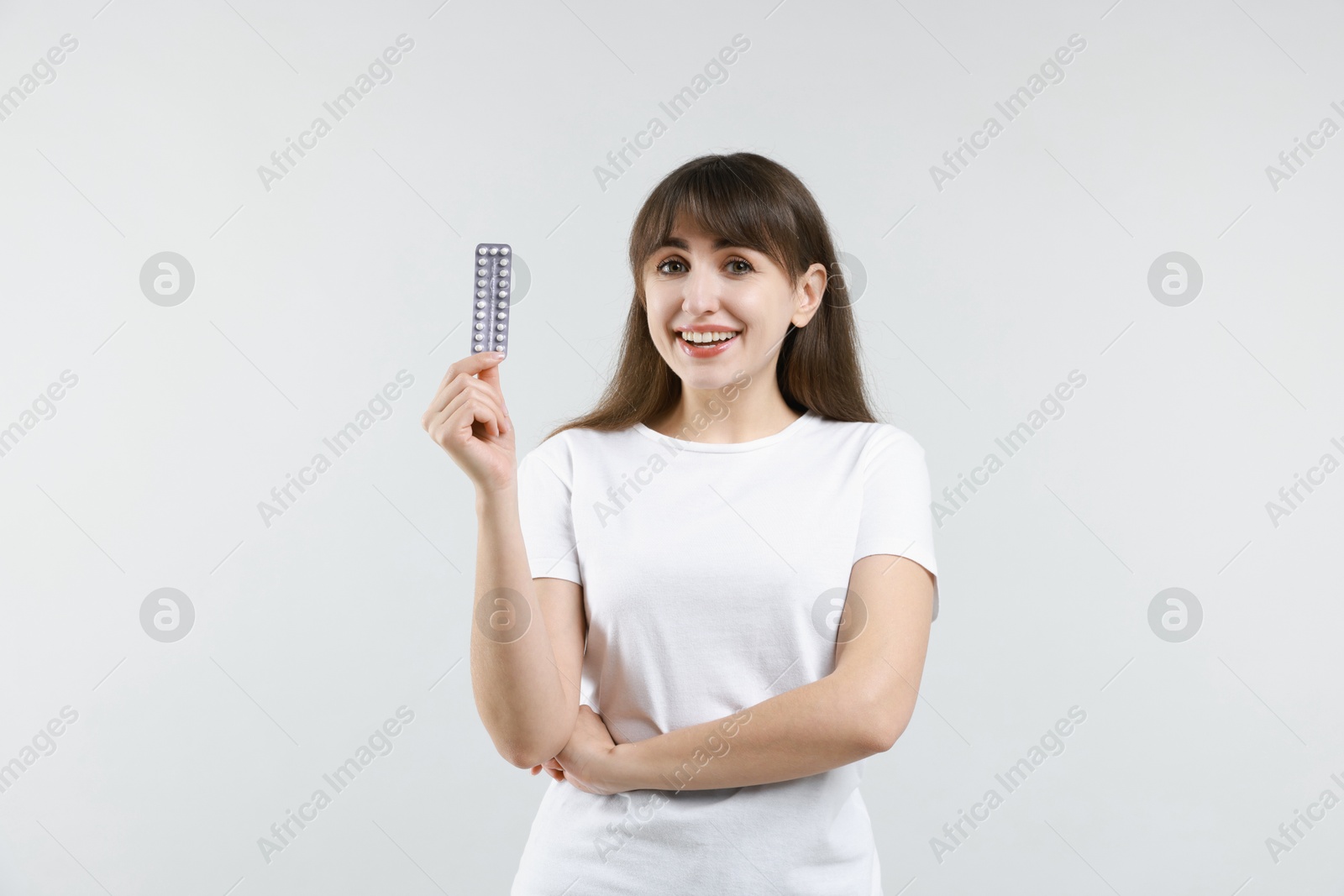 Photo of Smiling woman with blister of contraceptive pills on light background