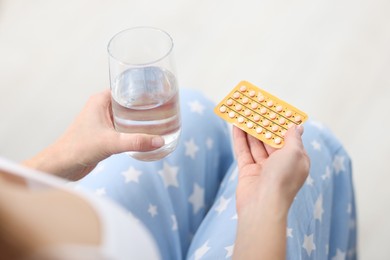 Photo of Woman with contraceptive pills and glass of water on light background, closeup