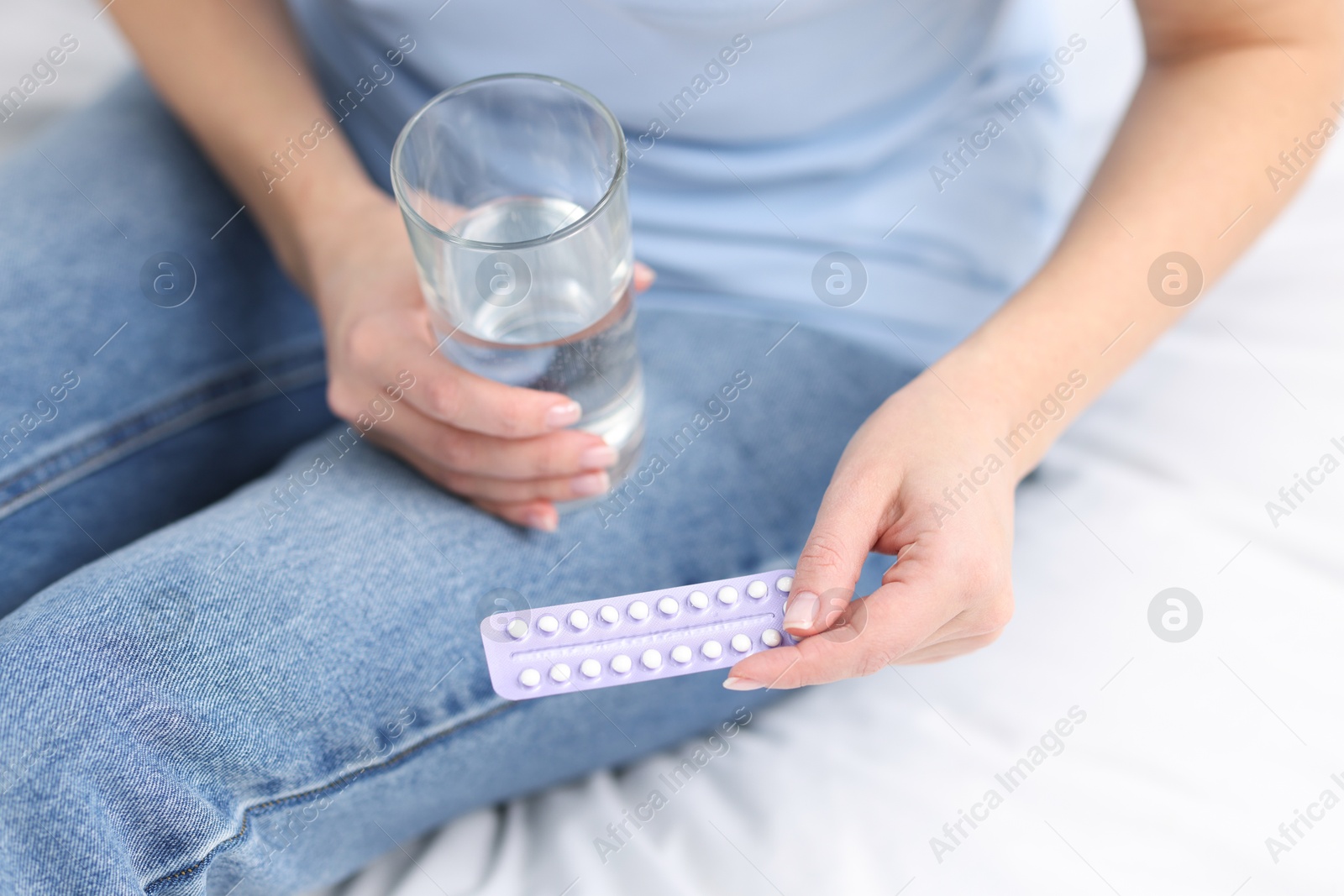 Photo of Woman with contraceptive pills and glass of water on bed, closeup