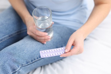 Photo of Woman with contraceptive pills and glass of water on bed, closeup