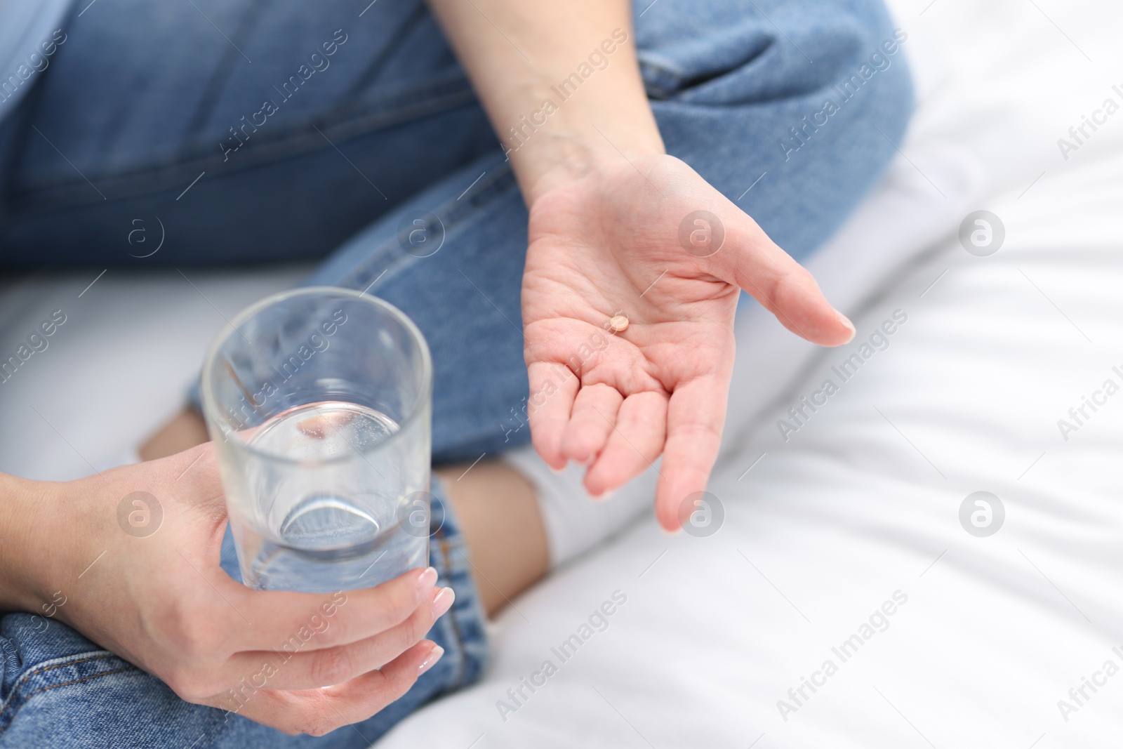 Photo of Woman with contraceptive pill and glass of water on bed, closeup