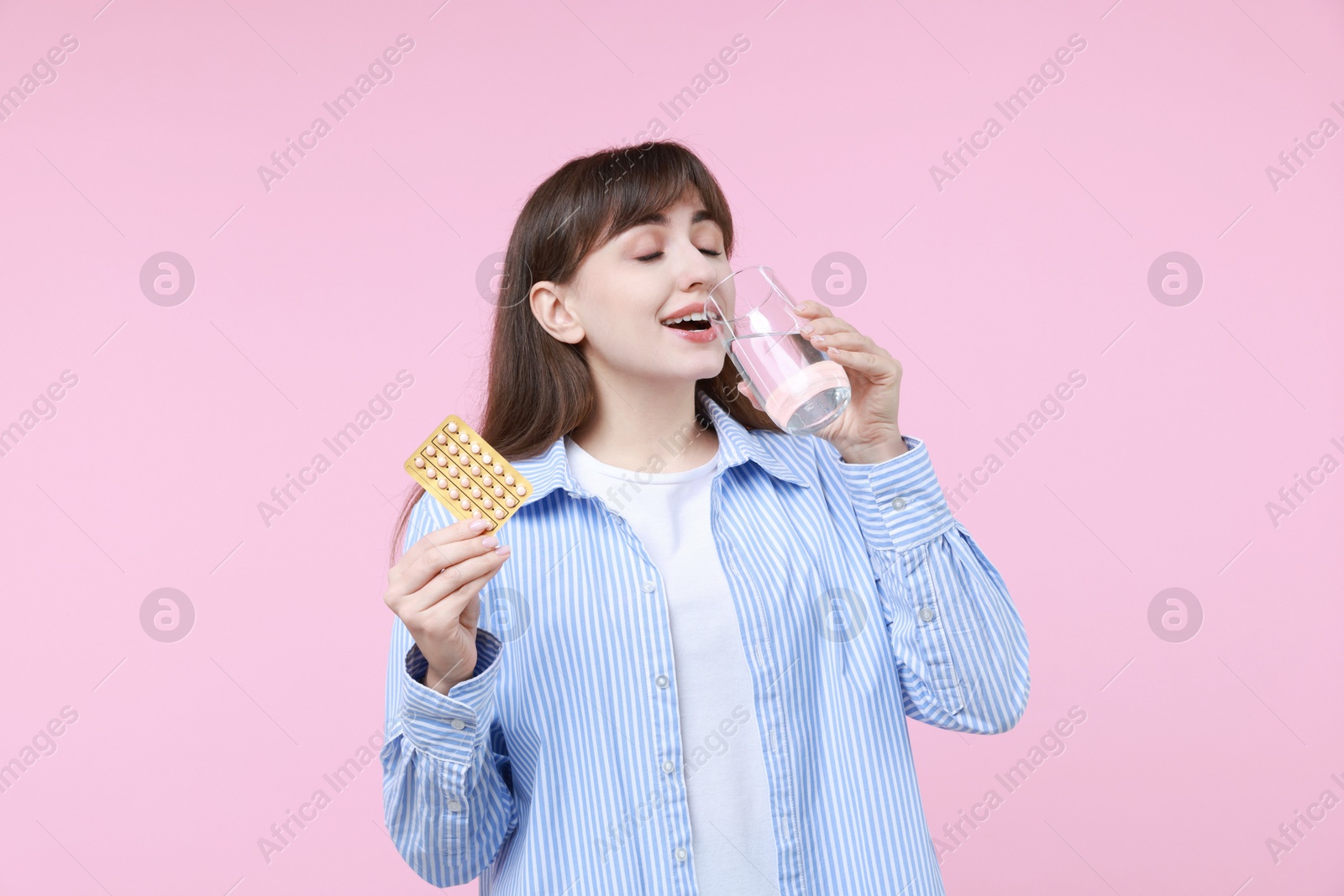 Photo of Young woman with contraceptive pills drinking water on pink background