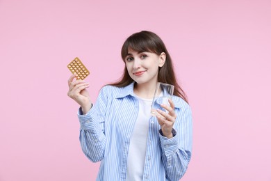 Photo of Young woman with contraceptive pills and glass of water on pink background