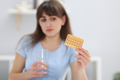 Photo of Woman with contraceptive pills and glass of water indoors, selective focus