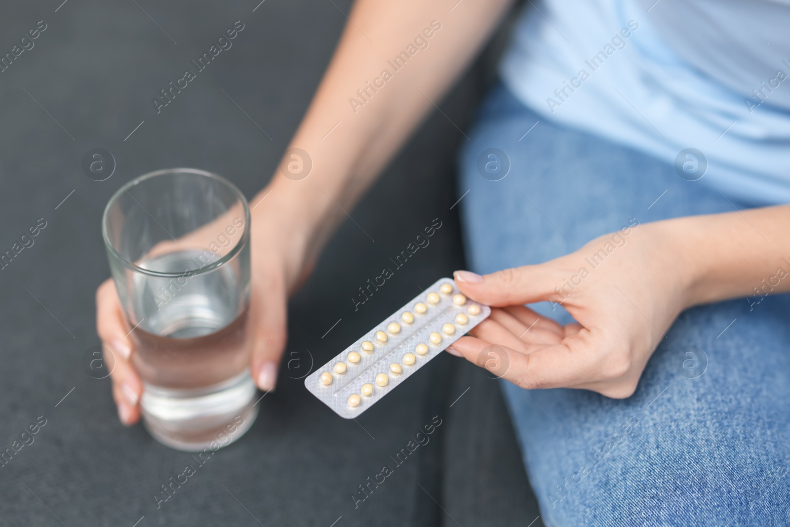 Photo of Woman with contraceptive pills and glass of water on sofa, closeup