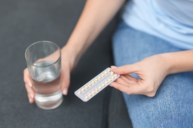 Photo of Woman with contraceptive pills and glass of water on sofa, closeup