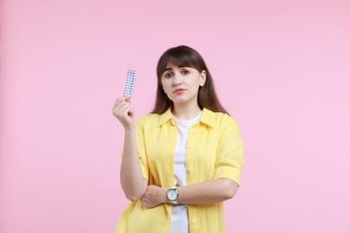 Photo of Upset woman with blister of contraceptive pills on pink background