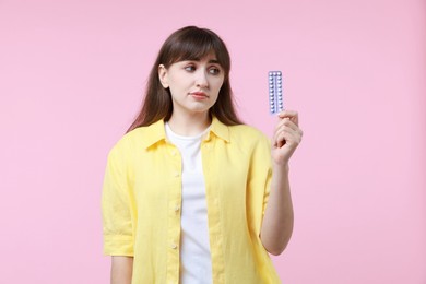 Upset woman with blister of contraceptive pills on pink background