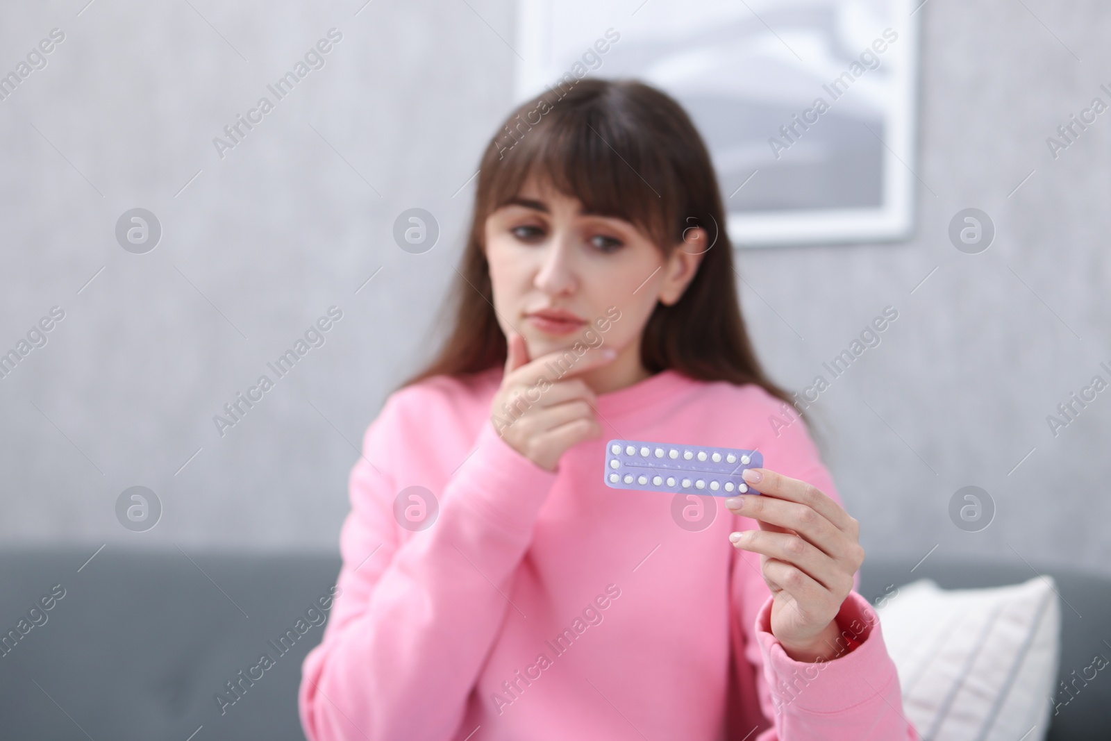 Photo of Upset woman with blister of contraceptive pills at home, selective focus