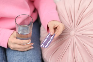 Photo of Woman with contraceptive pills and glass of water on sofa, closeup