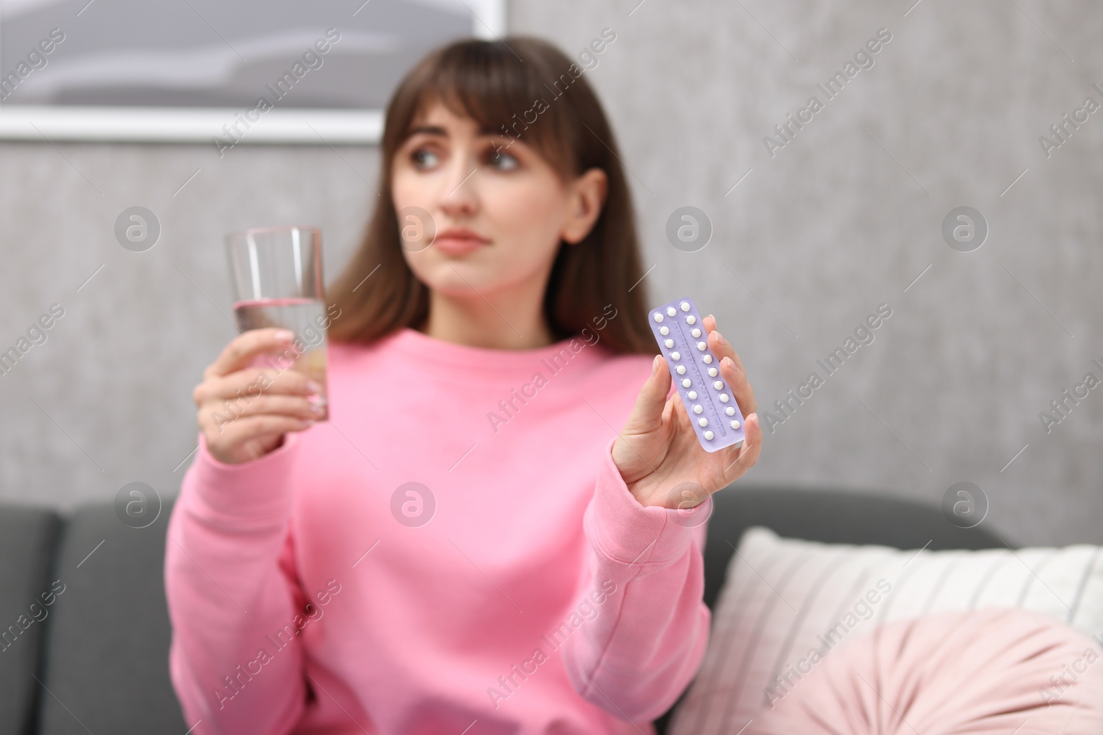 Photo of Woman with contraceptive pills and glass of water indoors, selective focus