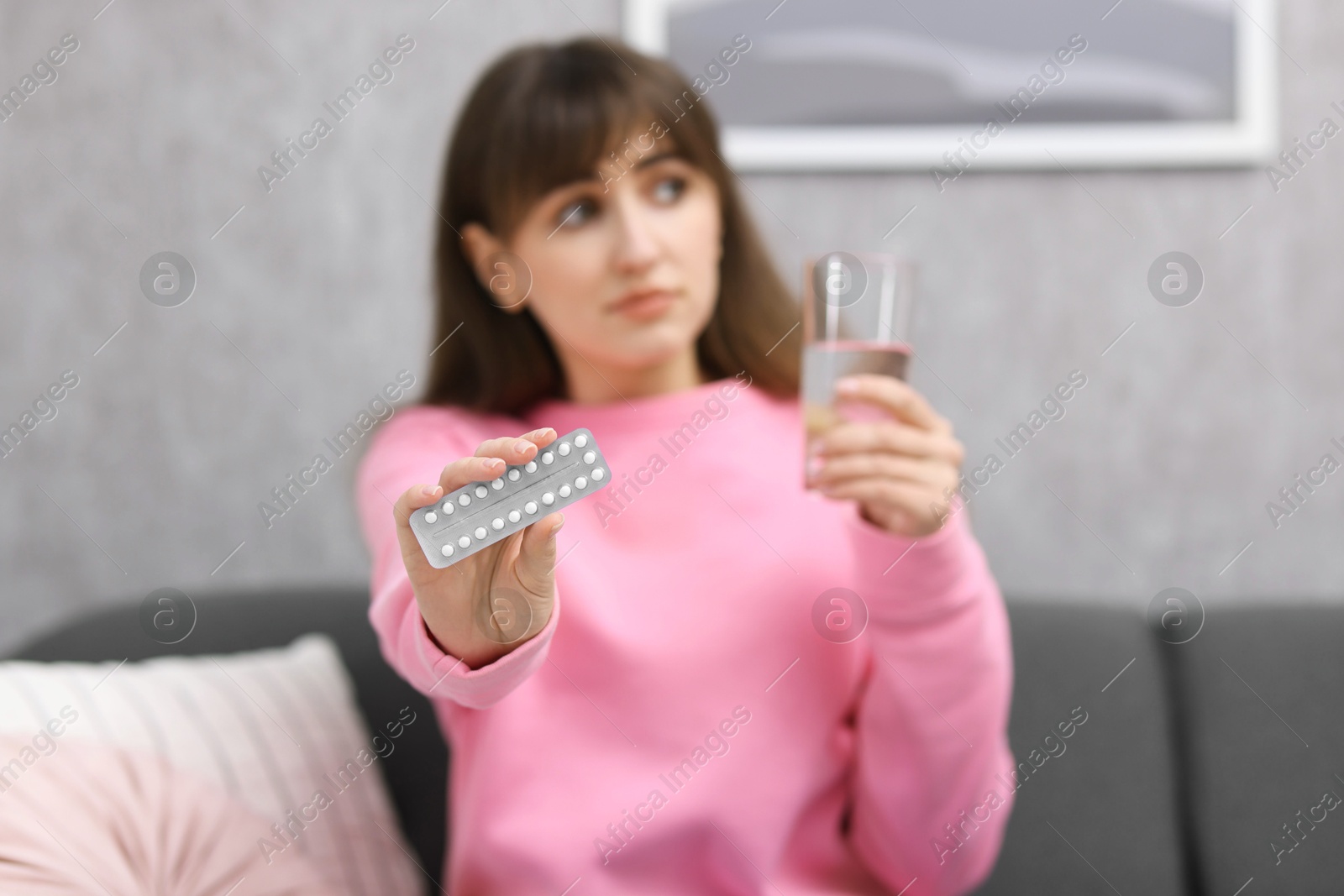 Photo of Woman with contraceptive pills and glass of water indoors, selective focus