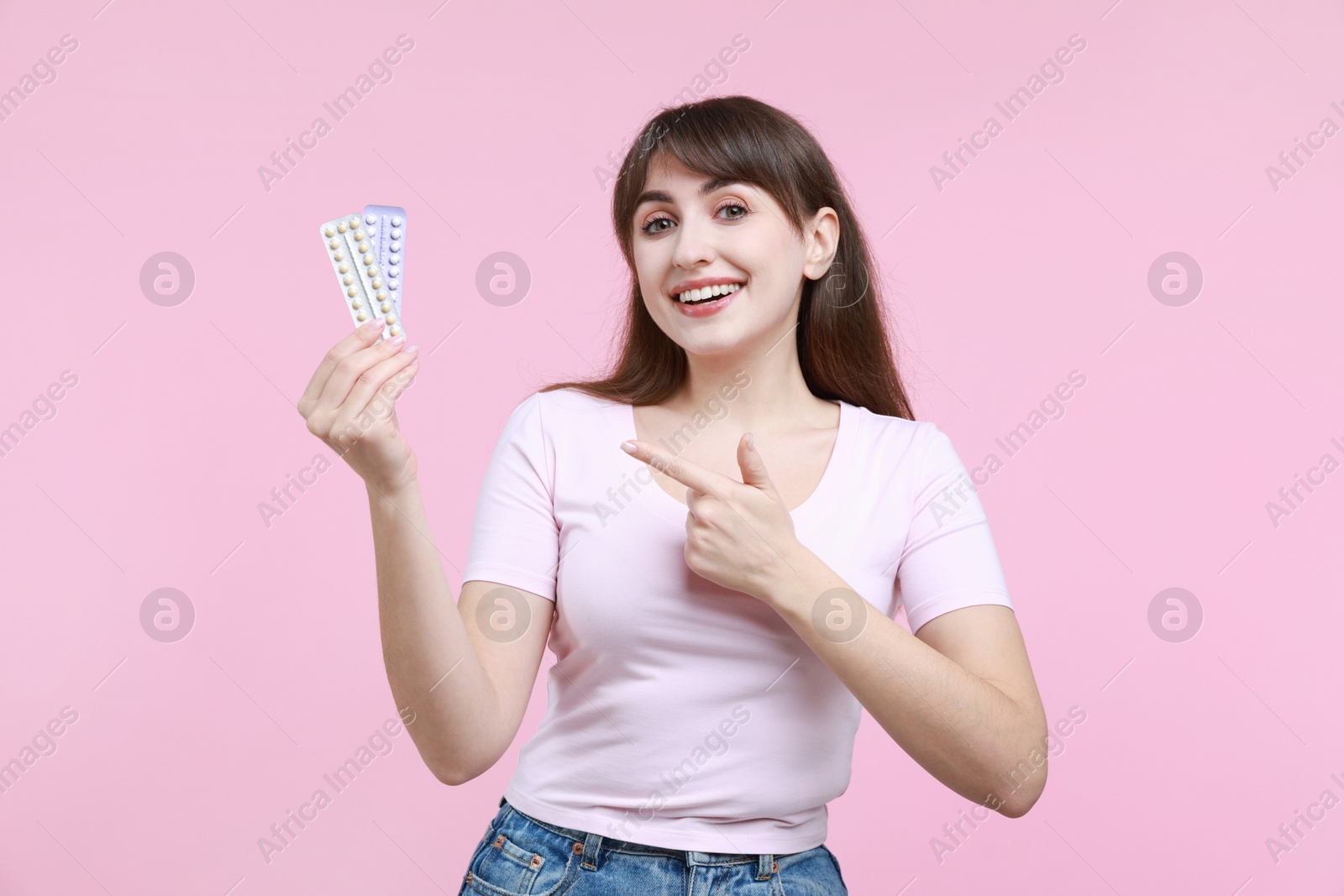 Photo of Smiling woman with blisters of contraceptive pills on pink background