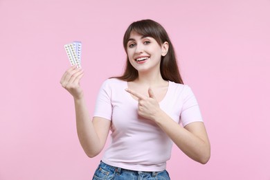 Photo of Smiling woman with blisters of contraceptive pills on pink background