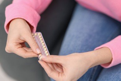 Photo of Woman taking contraceptive pill out from blister indoors, closeup