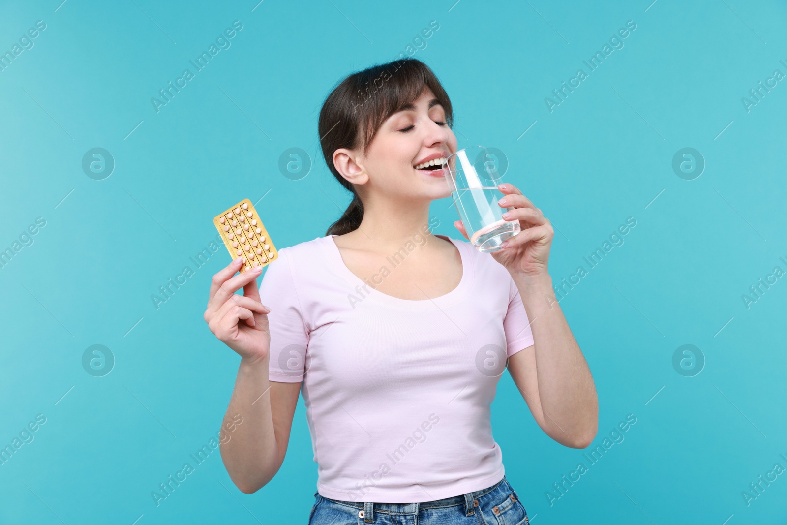 Photo of Young woman with contraceptive pills drinking water on light blue background