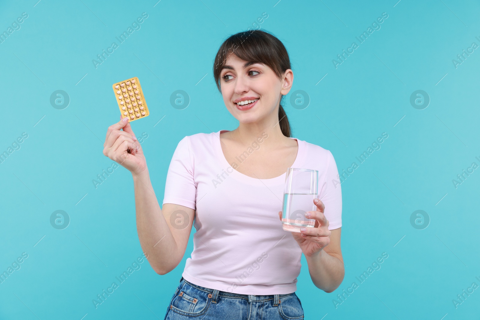 Photo of Smiling woman with contraceptive pills and glass of water on light blue background