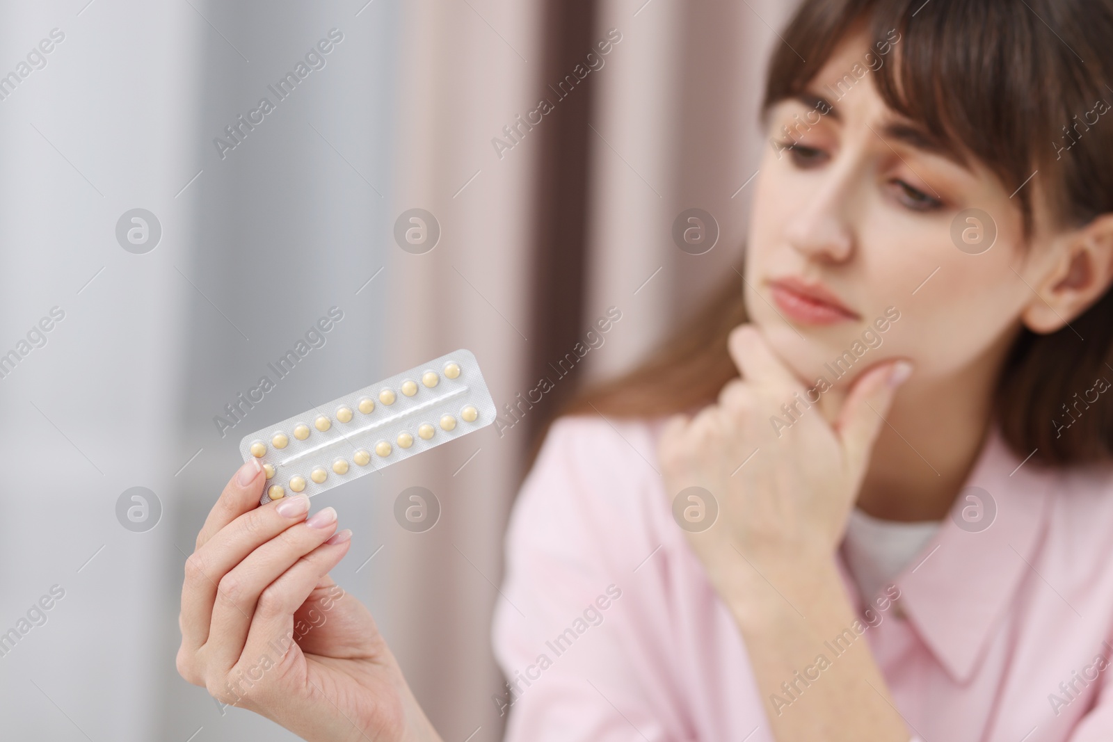 Photo of Upset woman with blister of contraceptive pills indoors, selective focus