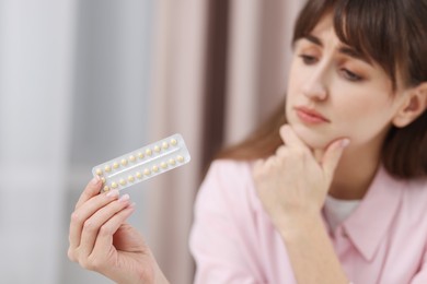 Photo of Upset woman with blister of contraceptive pills indoors, selective focus