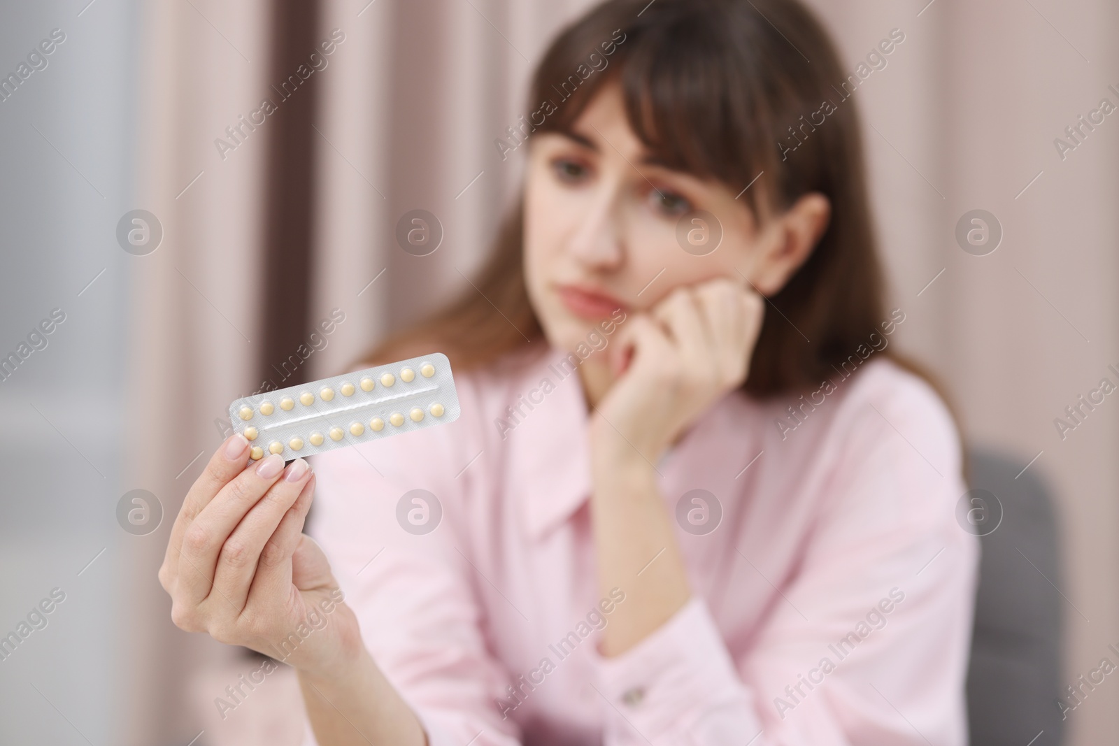 Photo of Upset woman with blister of contraceptive pills indoors, selective focus