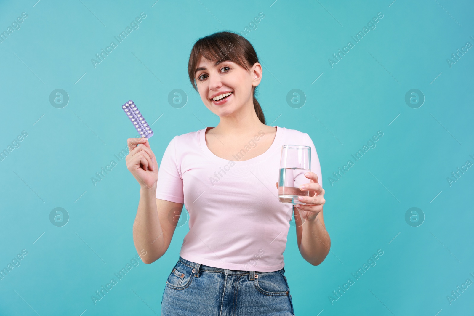 Photo of Smiling woman with contraceptive pills and glass of water on light blue background