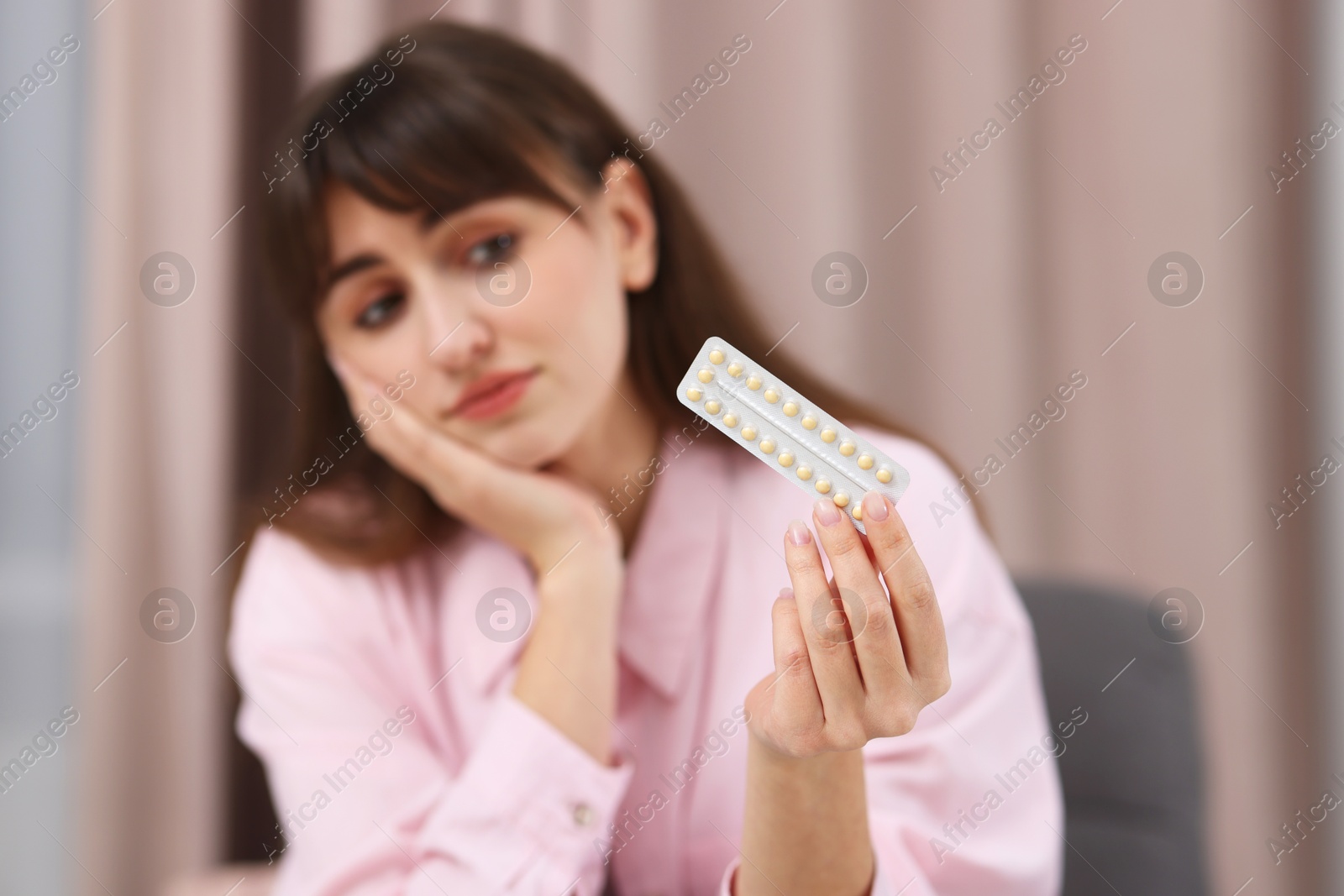 Photo of Upset woman with blister of contraceptive pills indoors, selective focus