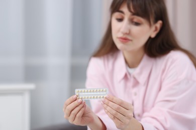 Upset woman with blister of contraceptive pills indoors, selective focus. Space for text