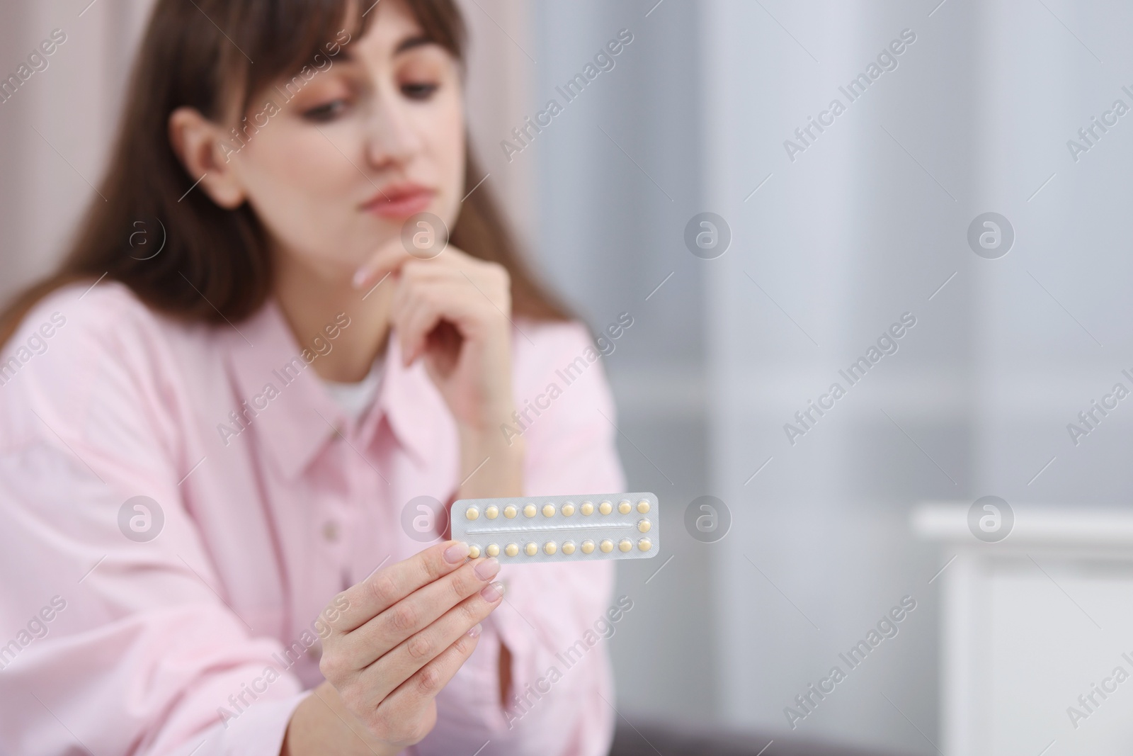 Photo of Upset woman with blister of contraceptive pills indoors, selective focus. Space for text