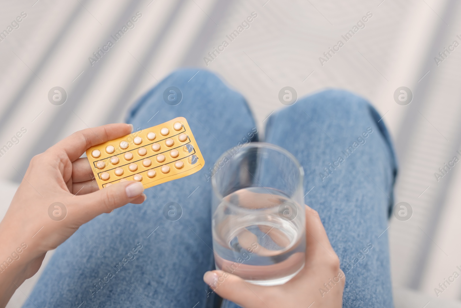 Photo of Woman with contraceptive pills and glass of water indoors, closeup