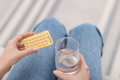 Photo of Woman with contraceptive pills and glass of water indoors, closeup