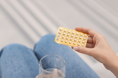 Photo of Woman with contraceptive pills and glass of water indoors, closeup