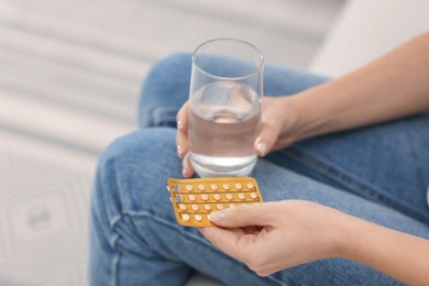 Photo of Woman with contraceptive pills and glass of water on sofa, closeup