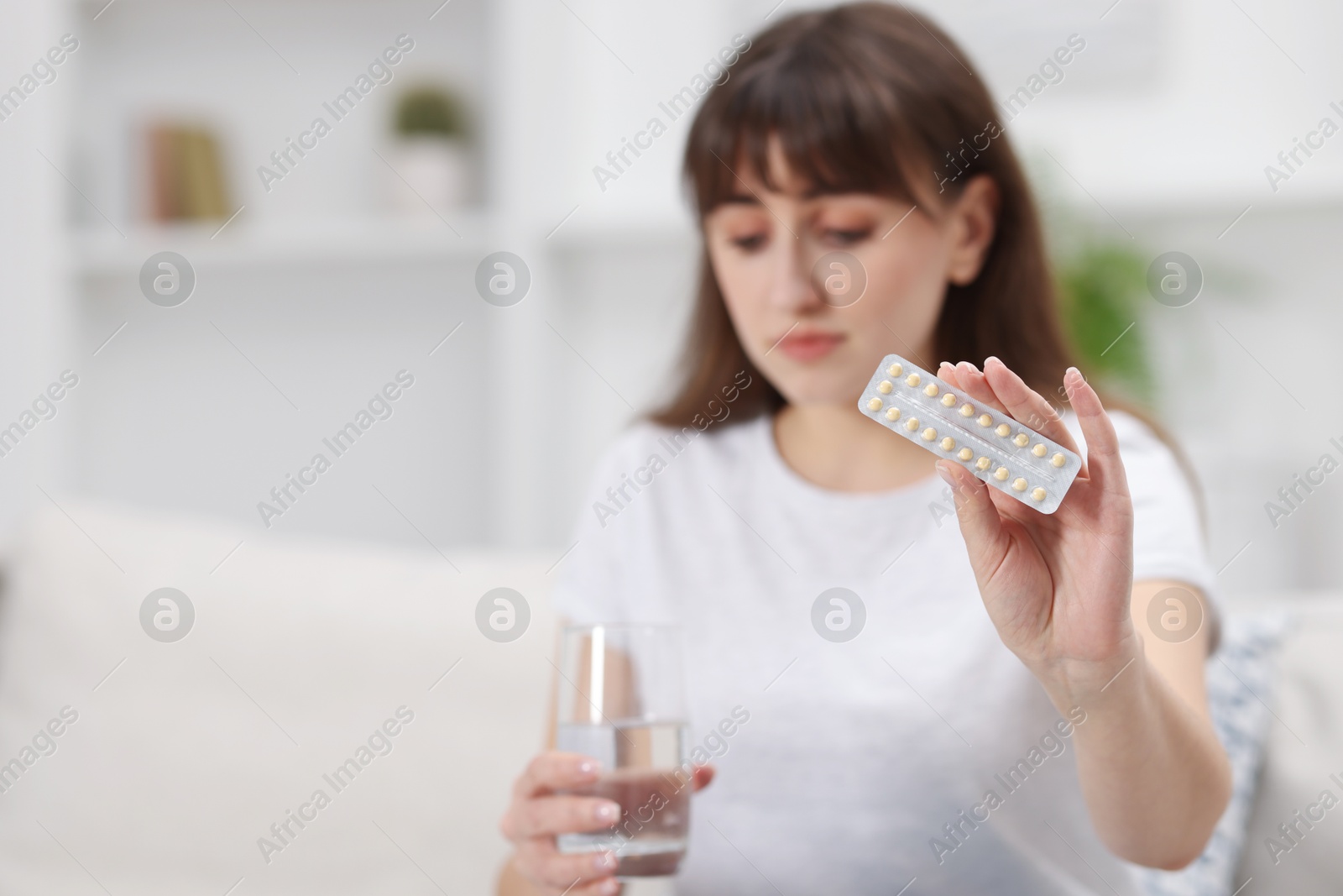 Photo of Upset woman with contraceptive pills and glass of water at home, selective focus. Space for text