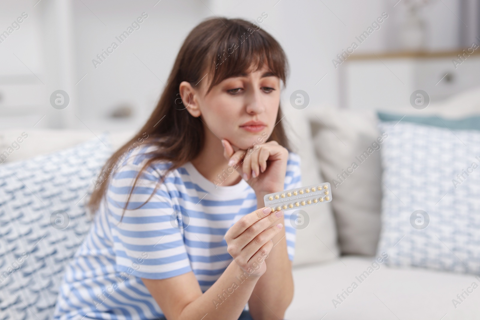 Photo of Upset woman with blister of contraceptive pills on sofa at home