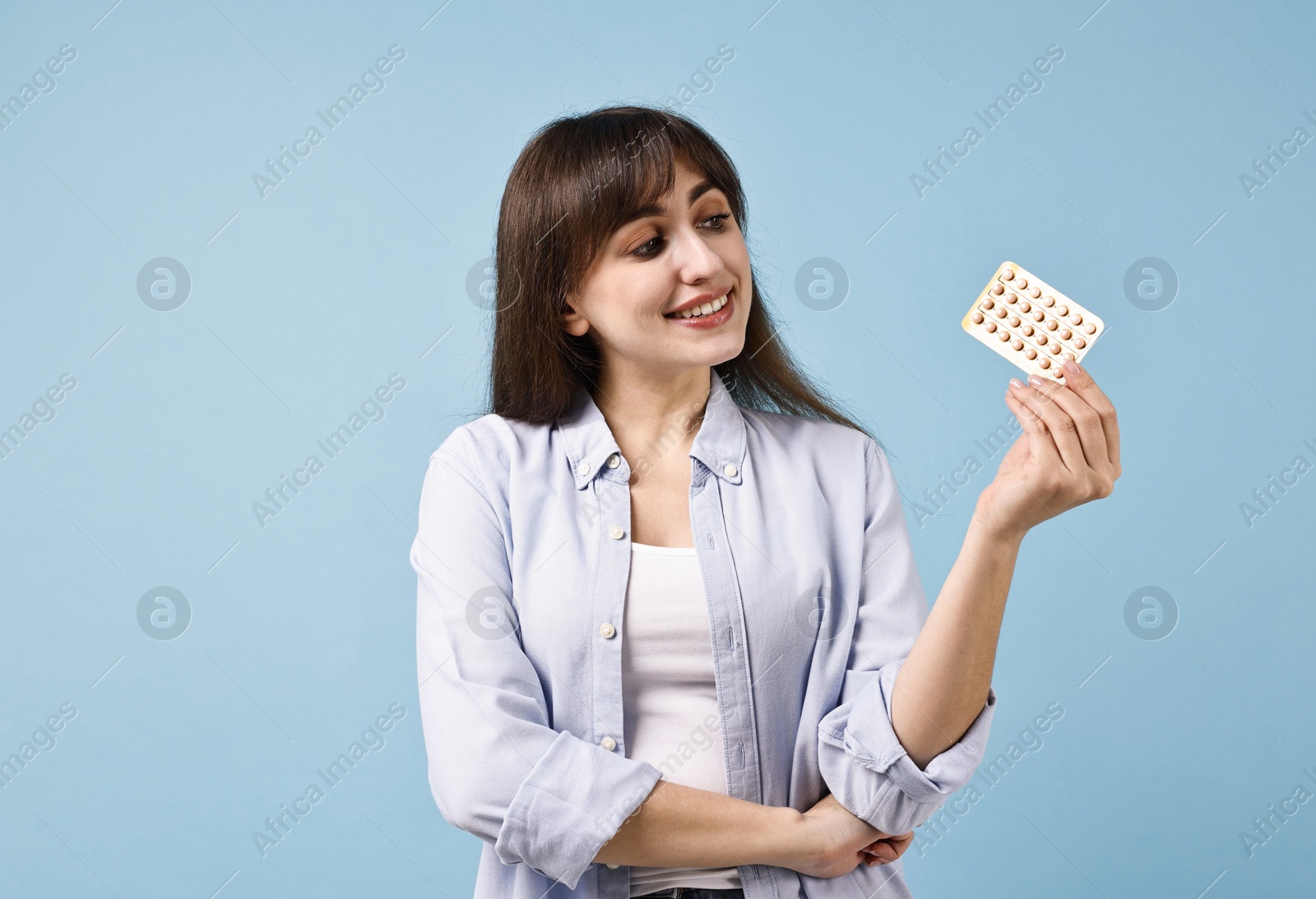 Photo of Smiling woman with blister of contraceptive pills on light blue background