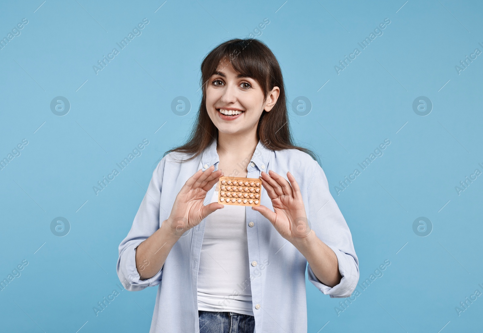 Photo of Smiling woman with blister of contraceptive pills on light blue background