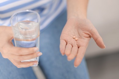 Photo of Woman with contraceptive pills and glass of water indoors, closeup