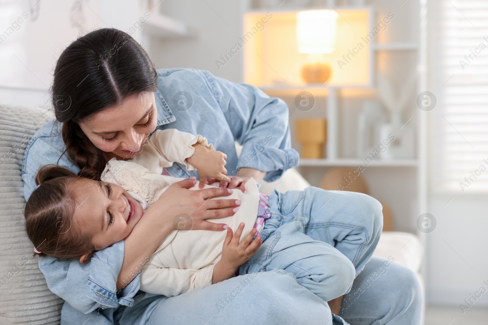 Photo of Happy mother having fun with her little daughter on sofa at home. Space for text