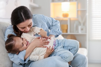 Photo of Happy mother having fun with her little daughter on sofa at home. Space for text