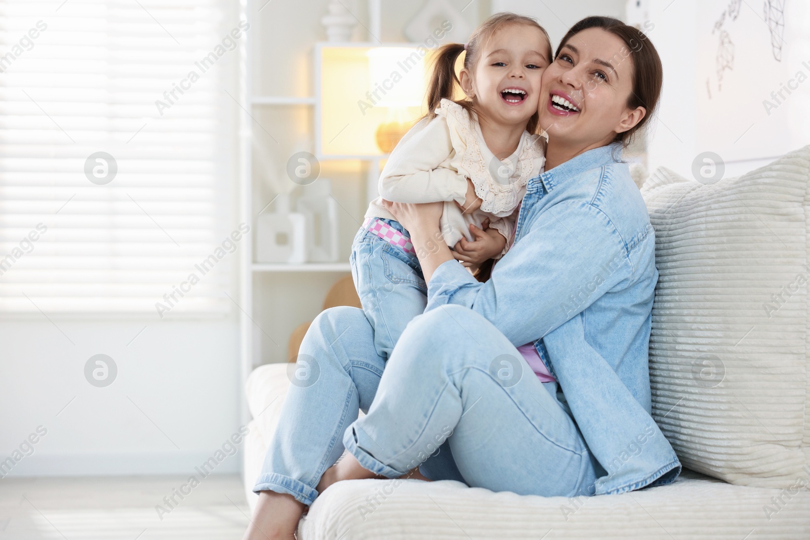 Photo of Happy mother having fun with her little daughter on sofa at home. Space for text