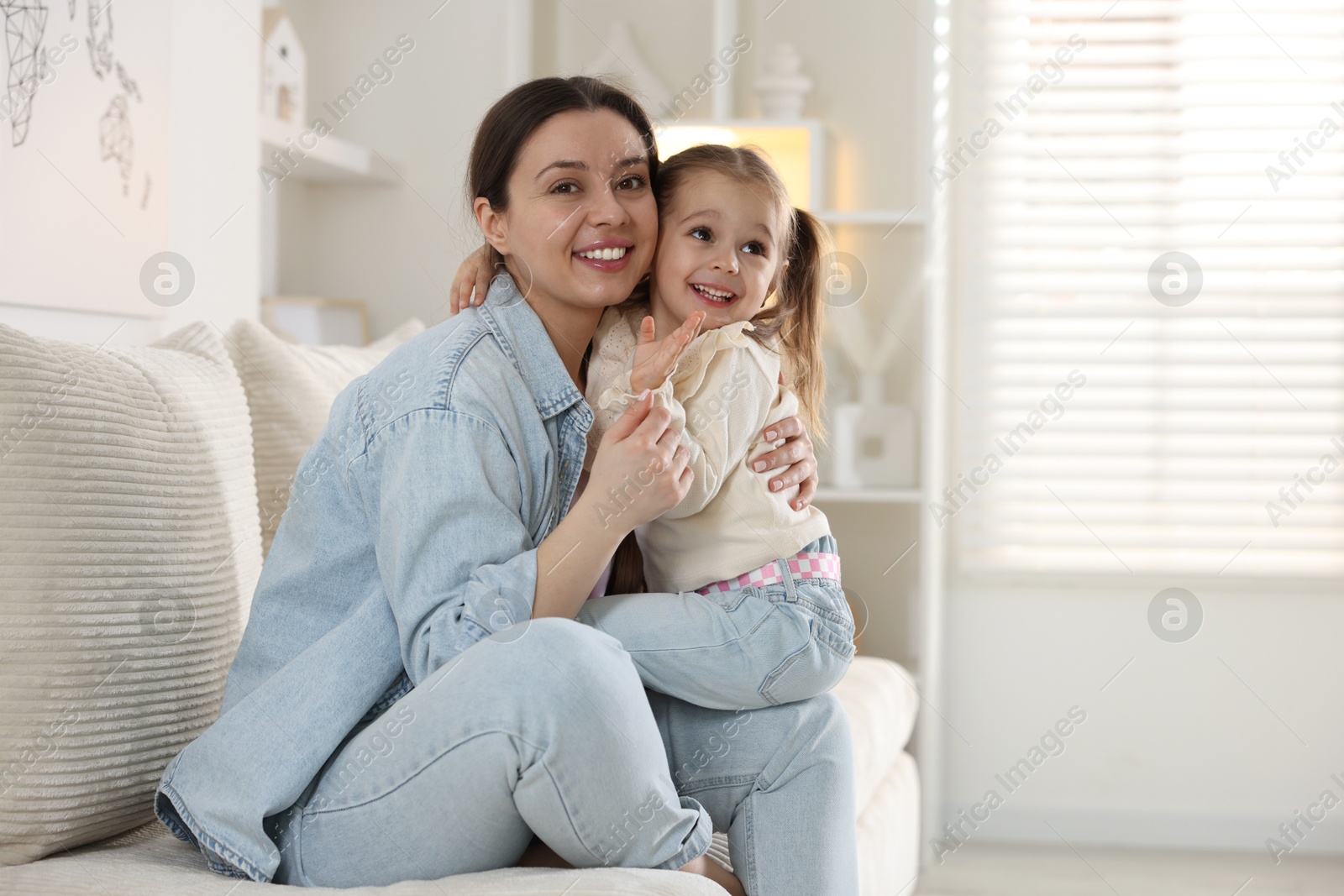 Photo of Happy mother with her cute little daughter on sofa at home. Space for text