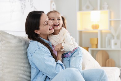 Happy mother having fun with her little daughter on sofa at home