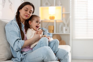 Photo of Beautiful mother with her little daughter on sofa at home. Space for text