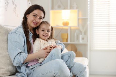 Photo of Beautiful mother with her little daughter on sofa at home. Space for text