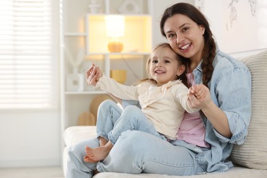 Photo of Happy mother having fun with her little daughter on sofa at home. Space for text