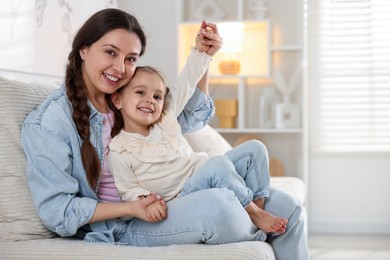 Photo of Happy mother having fun with her little daughter on sofa at home. Space for text