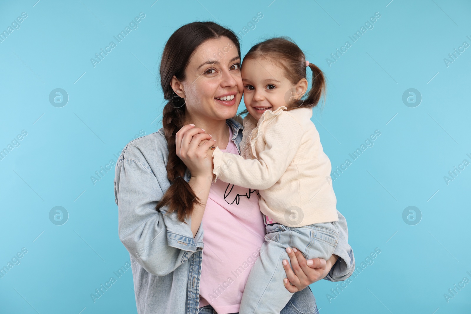 Photo of Portrait of happy mother with her cute daughter on light blue background