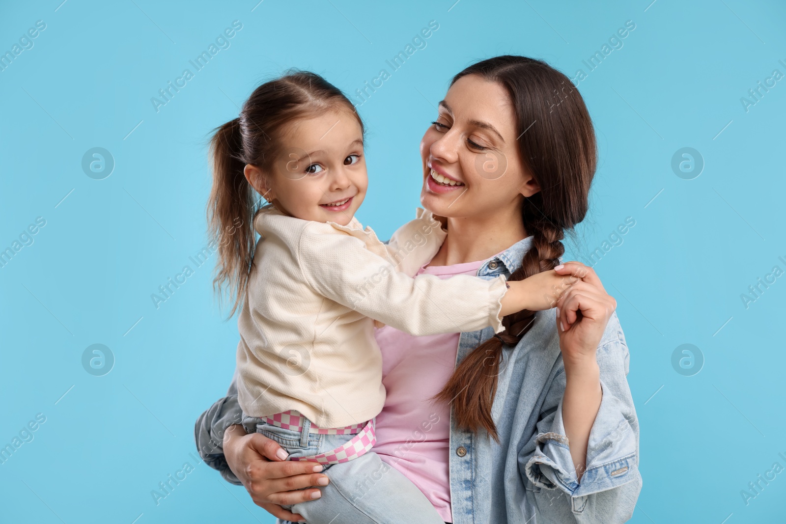 Photo of Portrait of happy mother with her cute daughter on light blue background